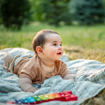 Happy baby boy playing on a picnic blanket in nature, surrounded by lush greenery. Joyful childhood ...