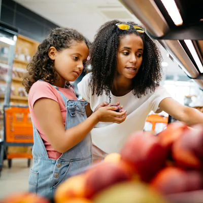 Black single mother and her daughter selecting fruits and vegetables from shelf while shopping in a supermarket