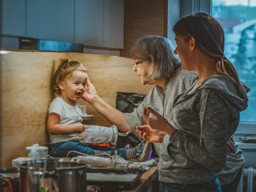 Photo of Grandmother and woman housewife, they feed the baby boy in the kitchen during the day. Youn...