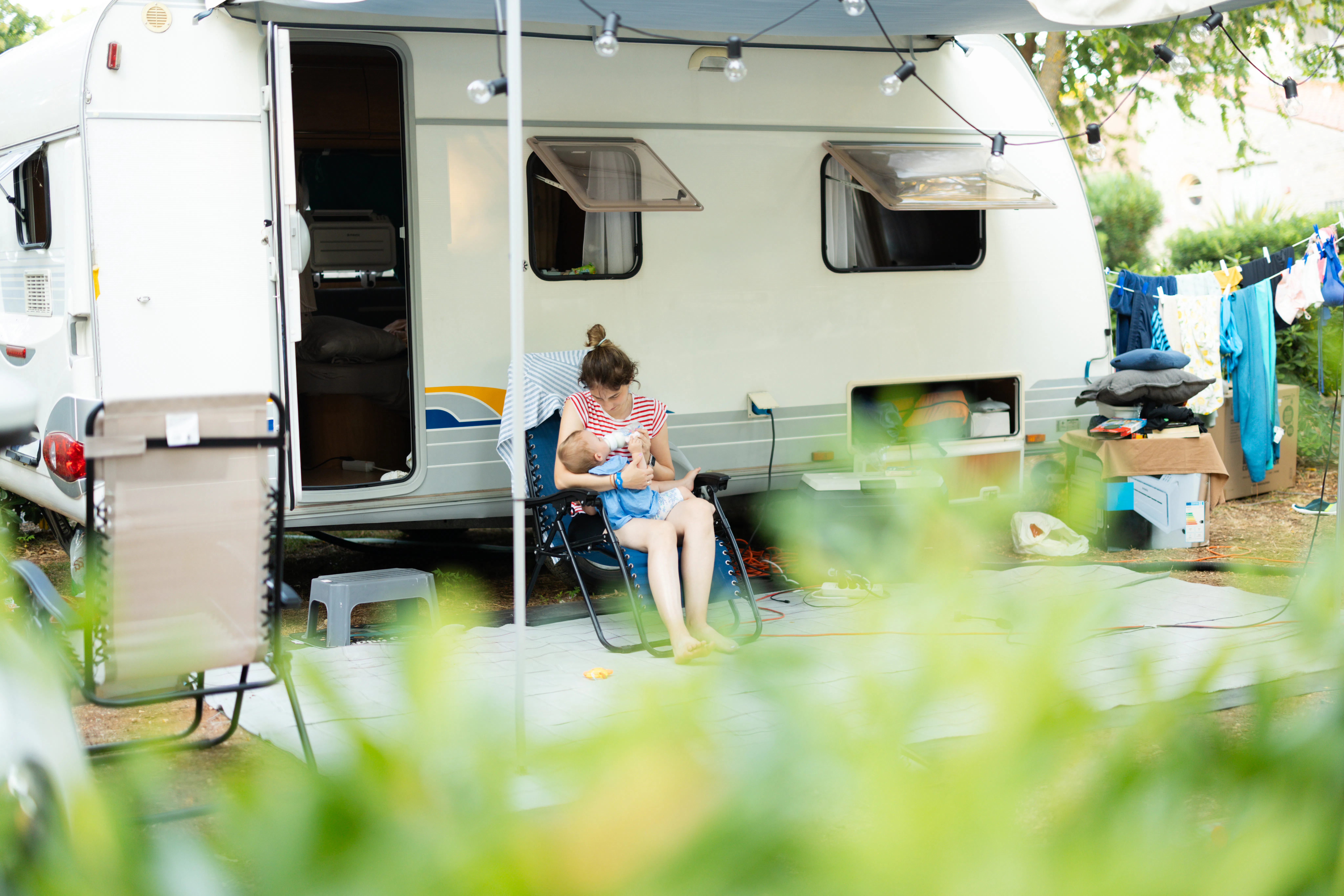Mother bottle feeding her baby while sitting in front of a travel trailer at a campsite