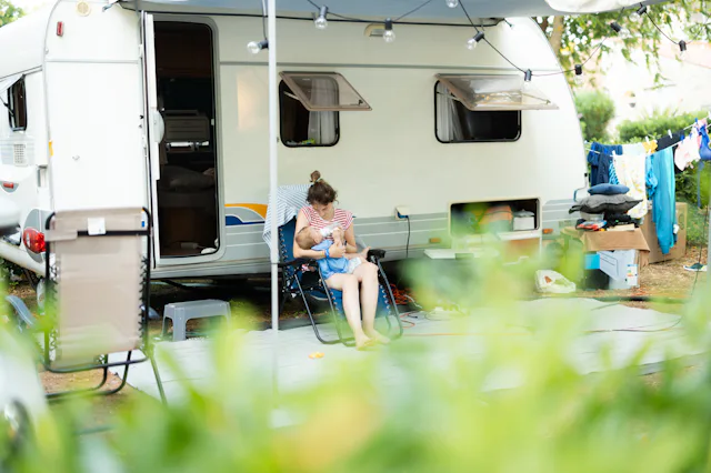 Mother bottle feeding her baby while sitting in front of a travel trailer at a campsite