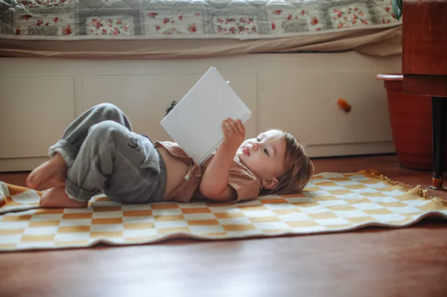 Toddler Lying on the Floor and Reading a Book at Home