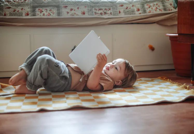 Toddler Lying on the Floor and Reading a Book at Home