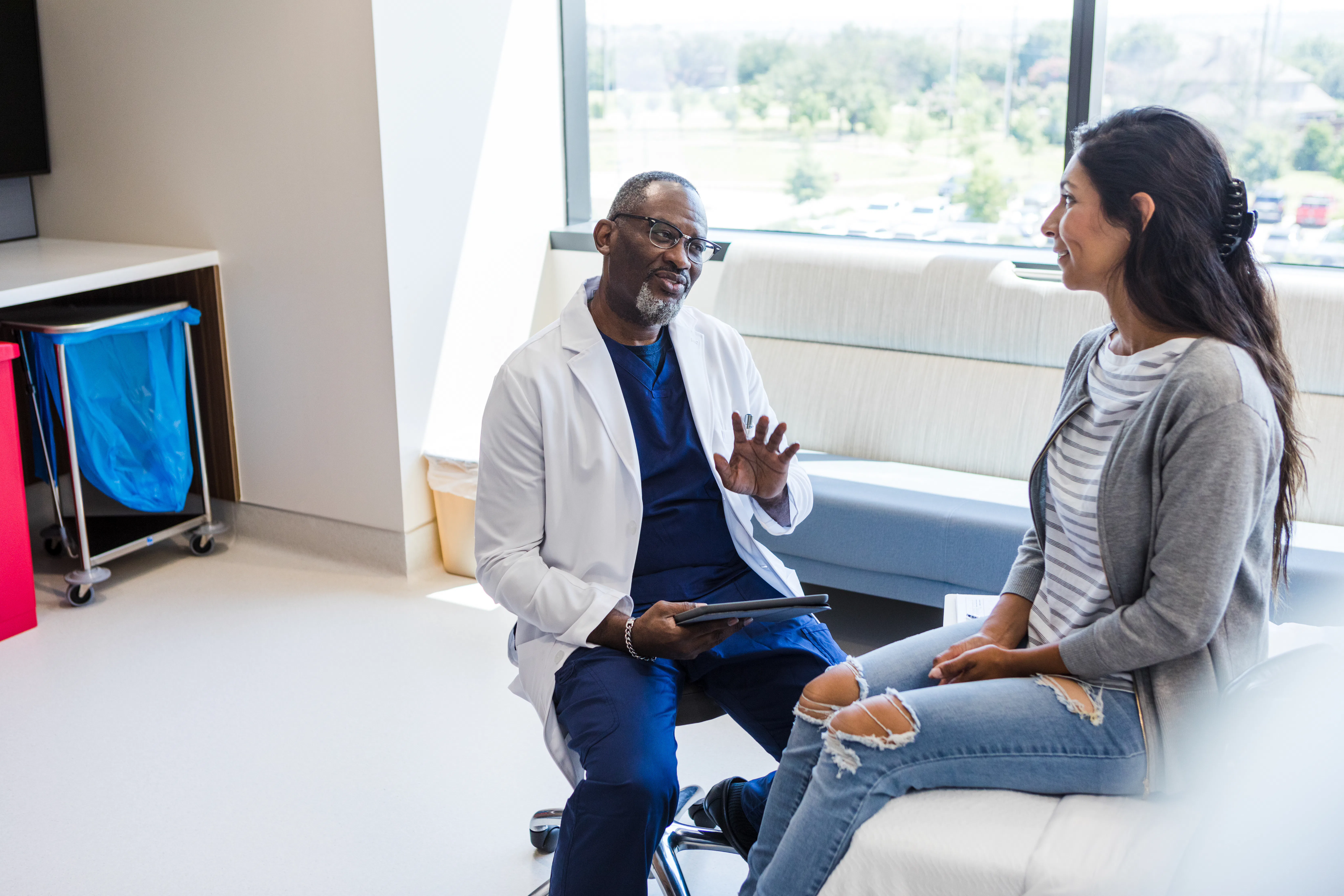 The young adult female patient smiles as the mature adult male doctor gives her advice.