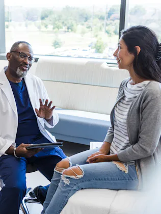 The young adult female patient smiles as the mature adult male doctor gives her advice.