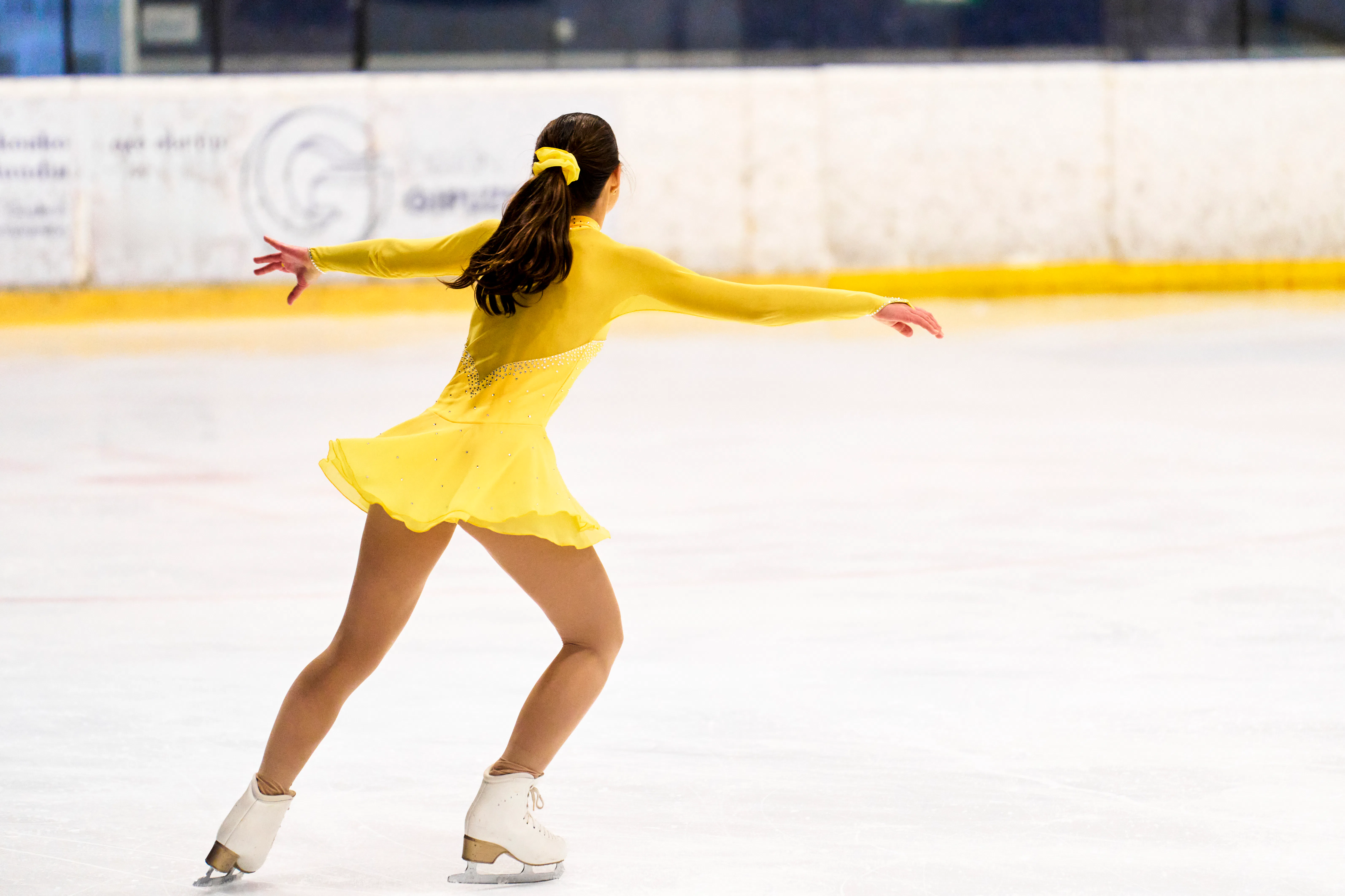 Young girl in yellow costume gracefully figure skating, enjoying her athletic performance on an indo...