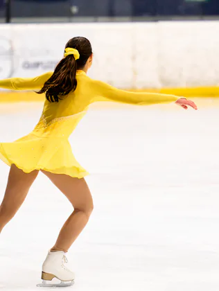 Young girl in yellow costume gracefully figure skating, enjoying her athletic performance on an indo...