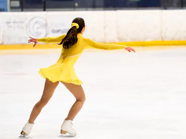 Young girl in yellow costume gracefully figure skating, enjoying her athletic performance on an indo...