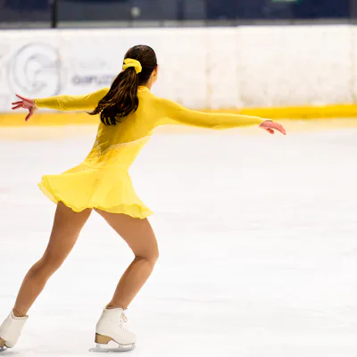 Young girl in yellow costume gracefully figure skating, enjoying her athletic performance on an indoor ice rink
