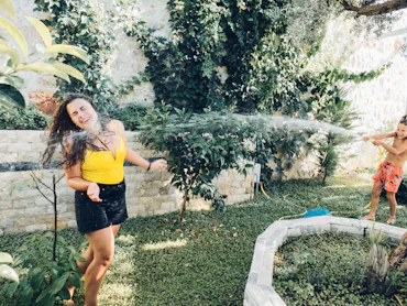 Happy young woman and cute child boy playing with water hose in garden. Weekend activity