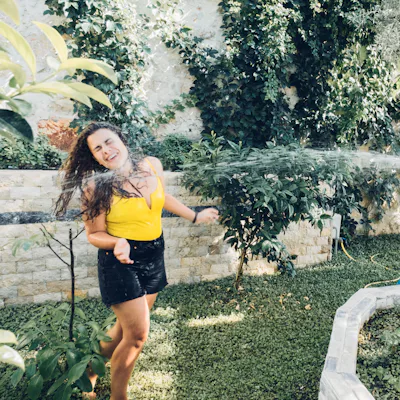 Happy young woman and cute child boy playing with water hose in garden. Weekend activity
