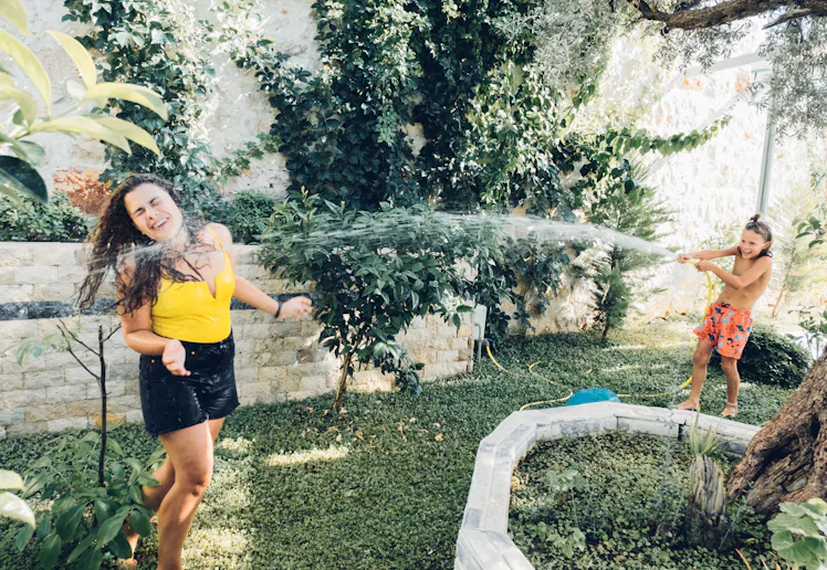 Happy young woman and cute child boy playing with water hose in garden. Weekend activity