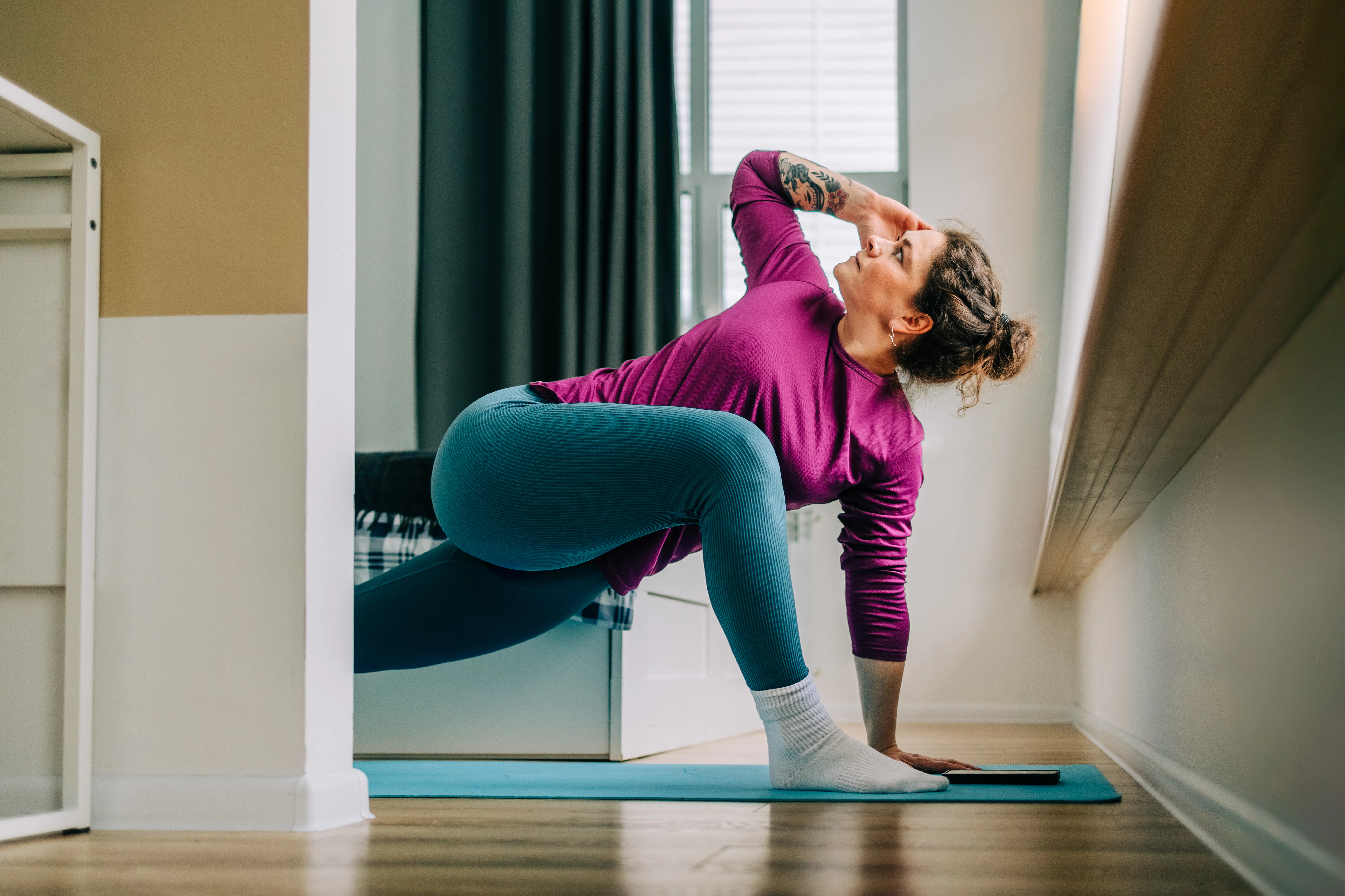 Mid adult woman practicing yoga at home stretching legs on exercise mat