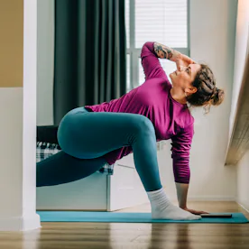 Mid adult woman practicing yoga at home stretching legs on exercise mat