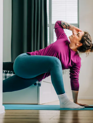 Mid adult woman practicing yoga at home stretching legs on exercise mat