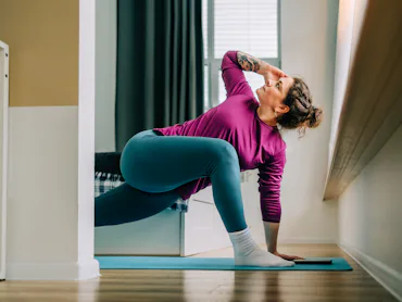 Mid adult woman practicing yoga at home stretching legs on exercise mat