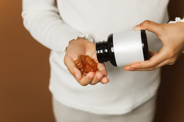 Small person in a light sweater pours brown gummy vitamins into their hand from a dark bottle, highl...
