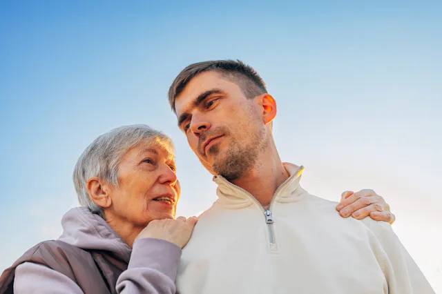 Mature mother and adult son sharing a moment of care and support under blue sky