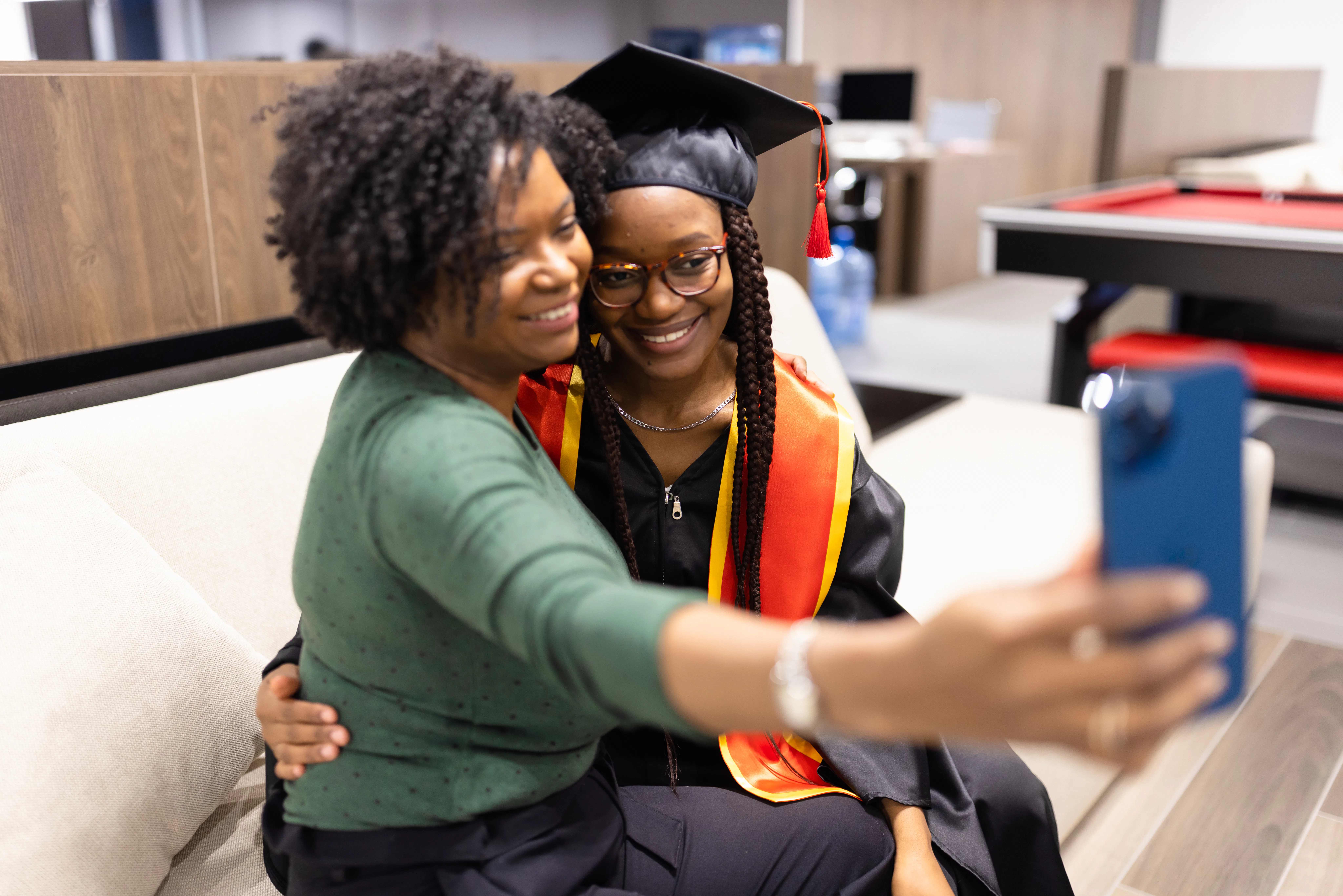 A proud mother takes a selfie with her daughter in graduation attire, capturing a joyful and memorab...