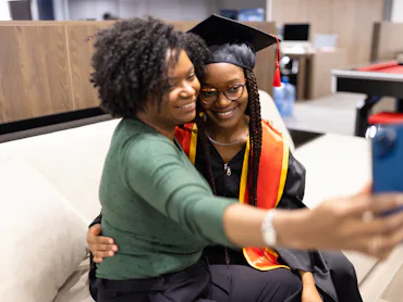 A proud mother takes a selfie with her daughter in graduation attire, capturing a joyful and memorab...
