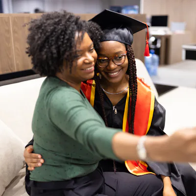 A proud mother takes a selfie with her daughter in graduation attire, capturing a joyful and memorable moment.