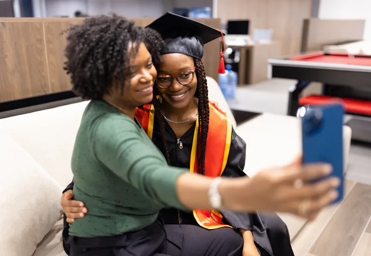 A proud mother takes a selfie with her daughter in graduation attire, capturing a joyful and memorab...