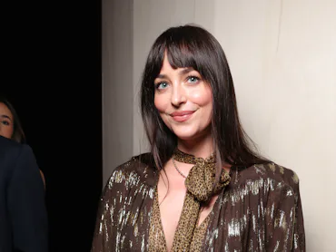 Dakota Johnson at a fashion show, posing against a wall
