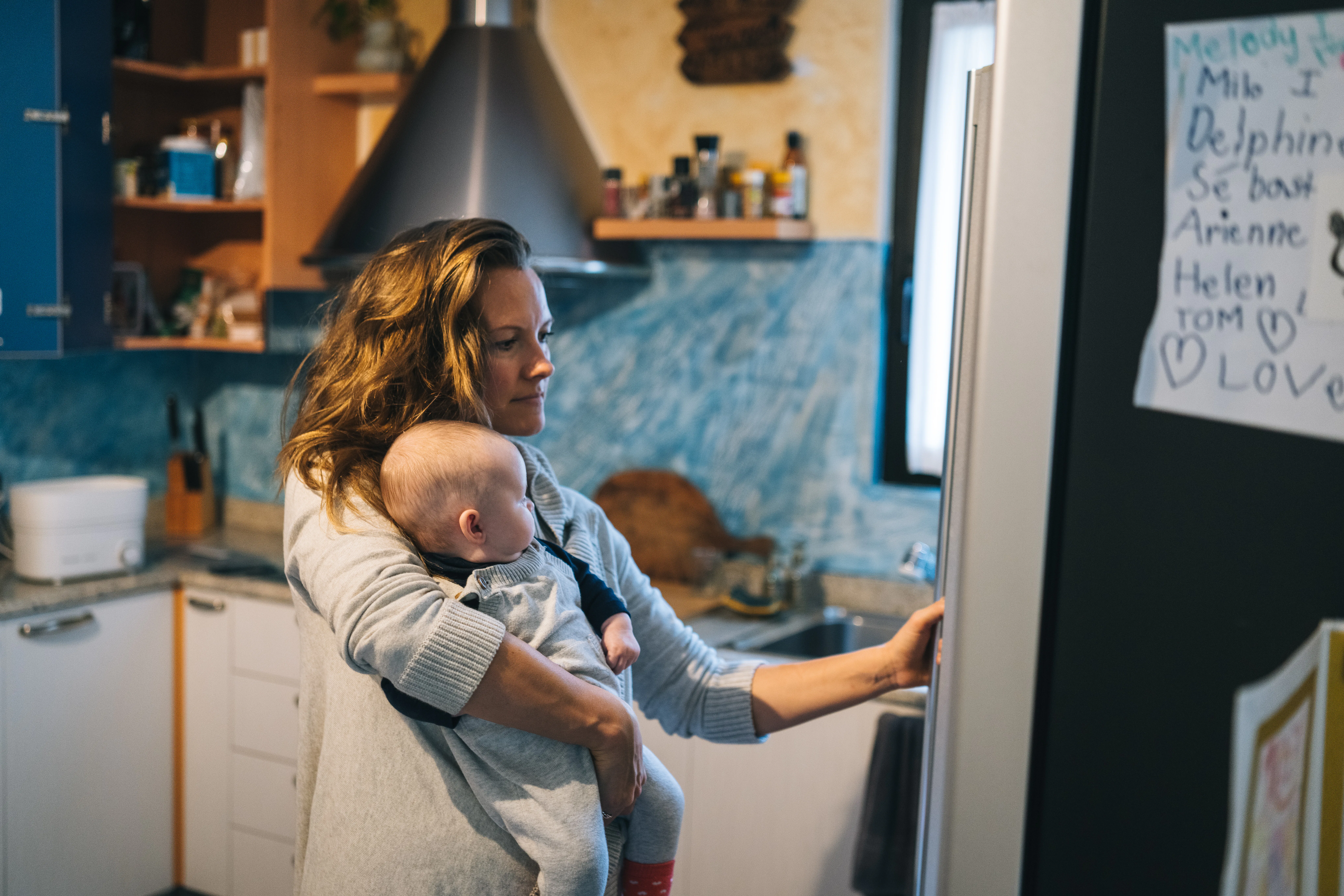 She is getting something from fridge while holding baby