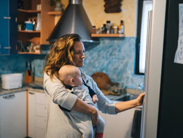 She is getting something from fridge while holding baby
