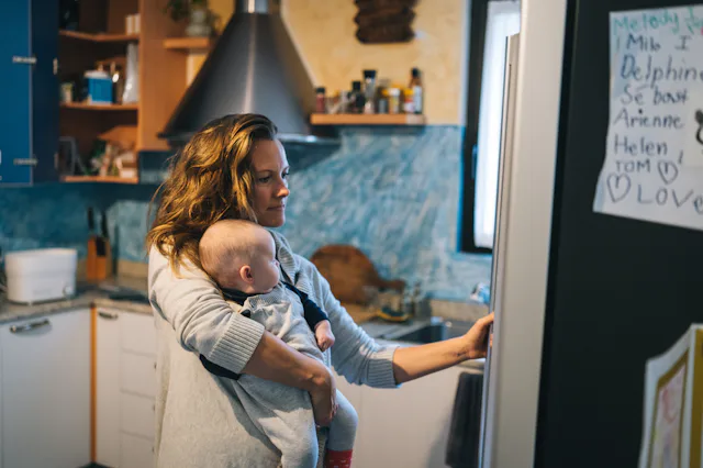 She is getting something from fridge while holding baby