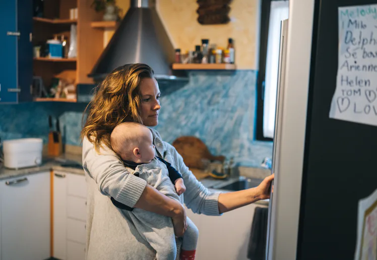 She is getting something from fridge while holding baby