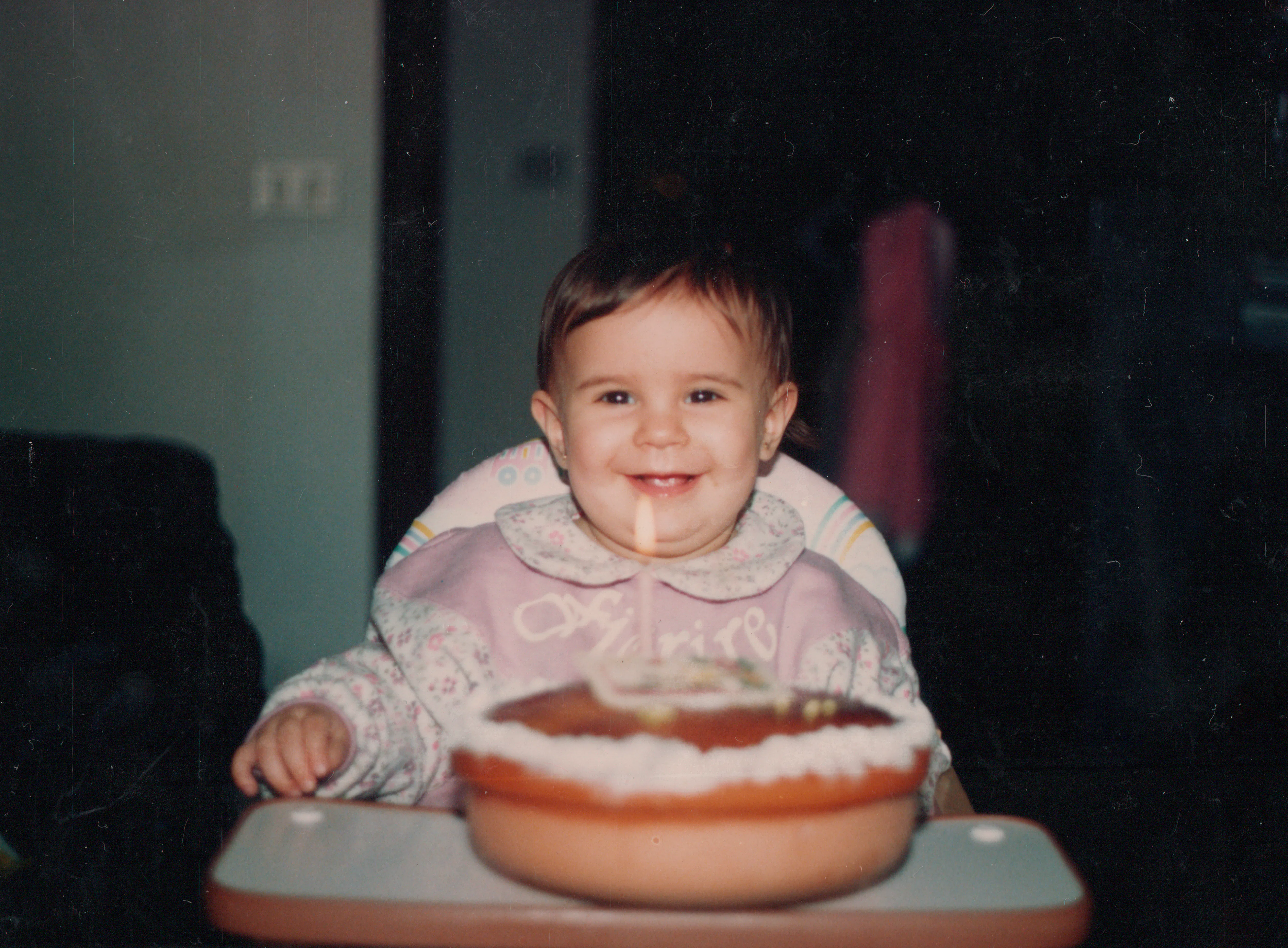 Happy baby girl during her first birthday party, with a candle on a homemade cake. 90's celebration....