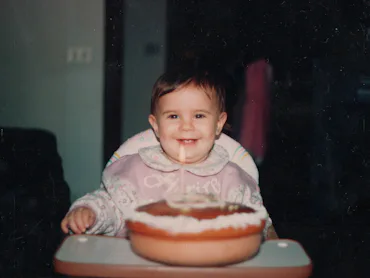 Happy baby girl during her first birthday party, with a candle on a homemade cake. 90's celebration....