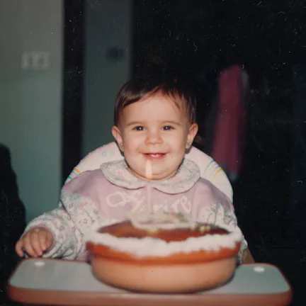 Happy baby girl during her first birthday party, with a candle on a homemade cake. 90's celebration....