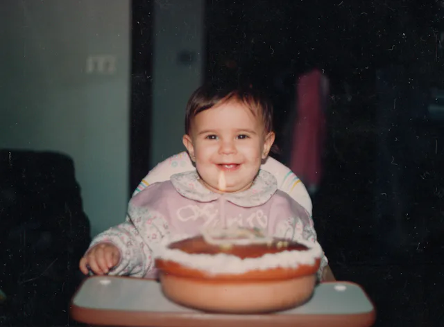 Happy baby girl during her first birthday party, with a candle on a homemade cake. 90's celebration....