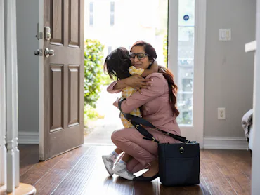 Toddler girl embracing mother in doorway as she gets home from work.