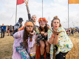 Group photo of four female friends blowing confetti into the camera lens. They are all dressed in vi...