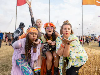 Group photo of four female friends blowing confetti into the camera lens. They are all dressed in vi...