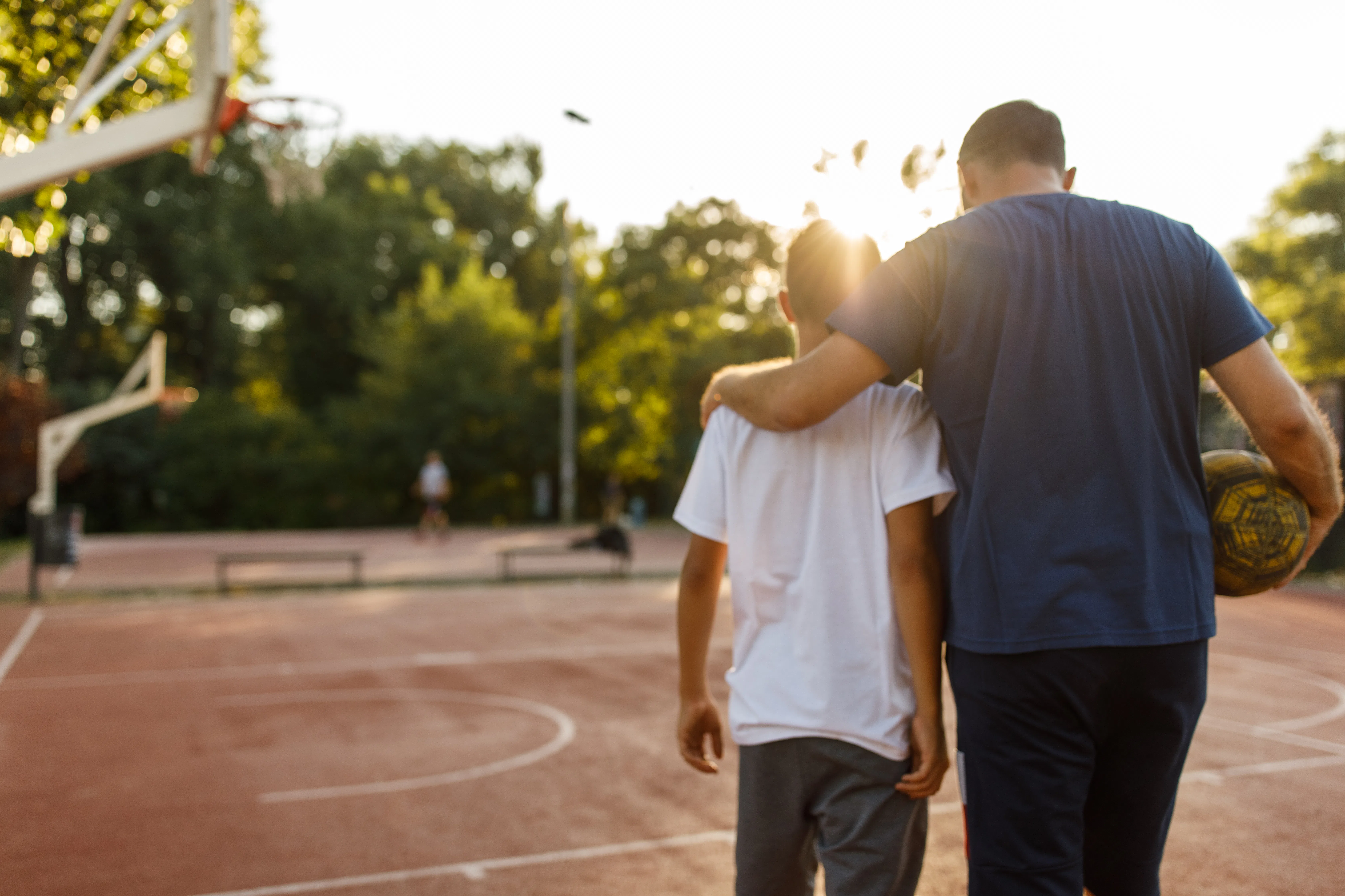 Embraced father and son walking towards the basketball court to play.