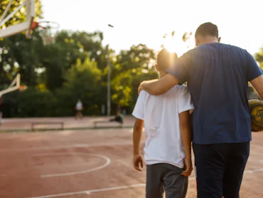 Embraced father and son walking towards the basketball court to play.