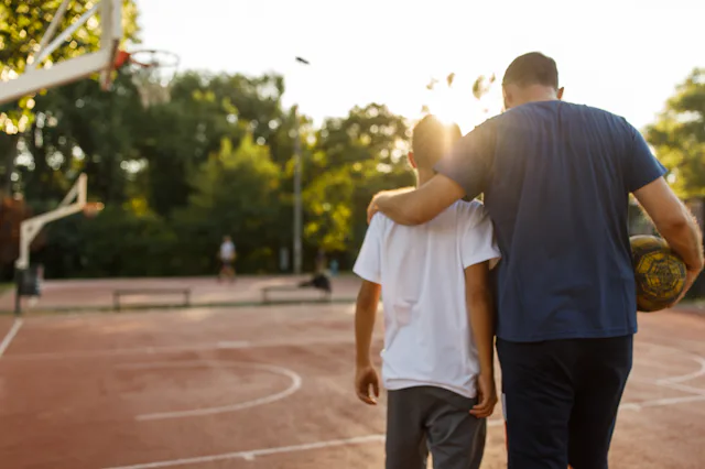 Embraced father and son walking towards the basketball court to play.