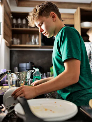 Teenage boy is helping in kitchen. The son is washing the dishes.Shot With Canon R5.