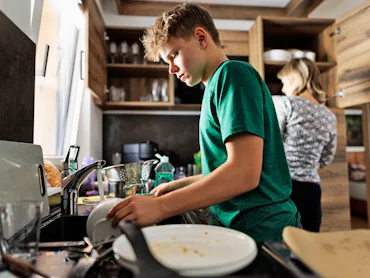 Teenage boy is helping in kitchen. The son is washing the dishes.Shot With Canon R5.