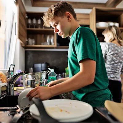 Teenage boy is helping in kitchen. The son is washing the dishes.Shot With Canon R5.
