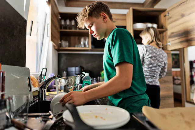 Teenage boy is helping in kitchen. The son is washing the dishes.Shot With Canon R5.