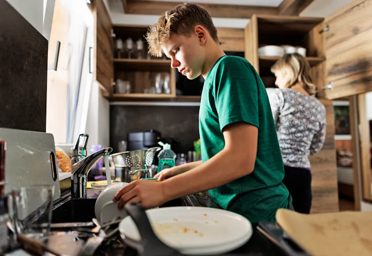 Teenage boy is helping in kitchen. The son is washing the dishes.Shot With Canon R5.