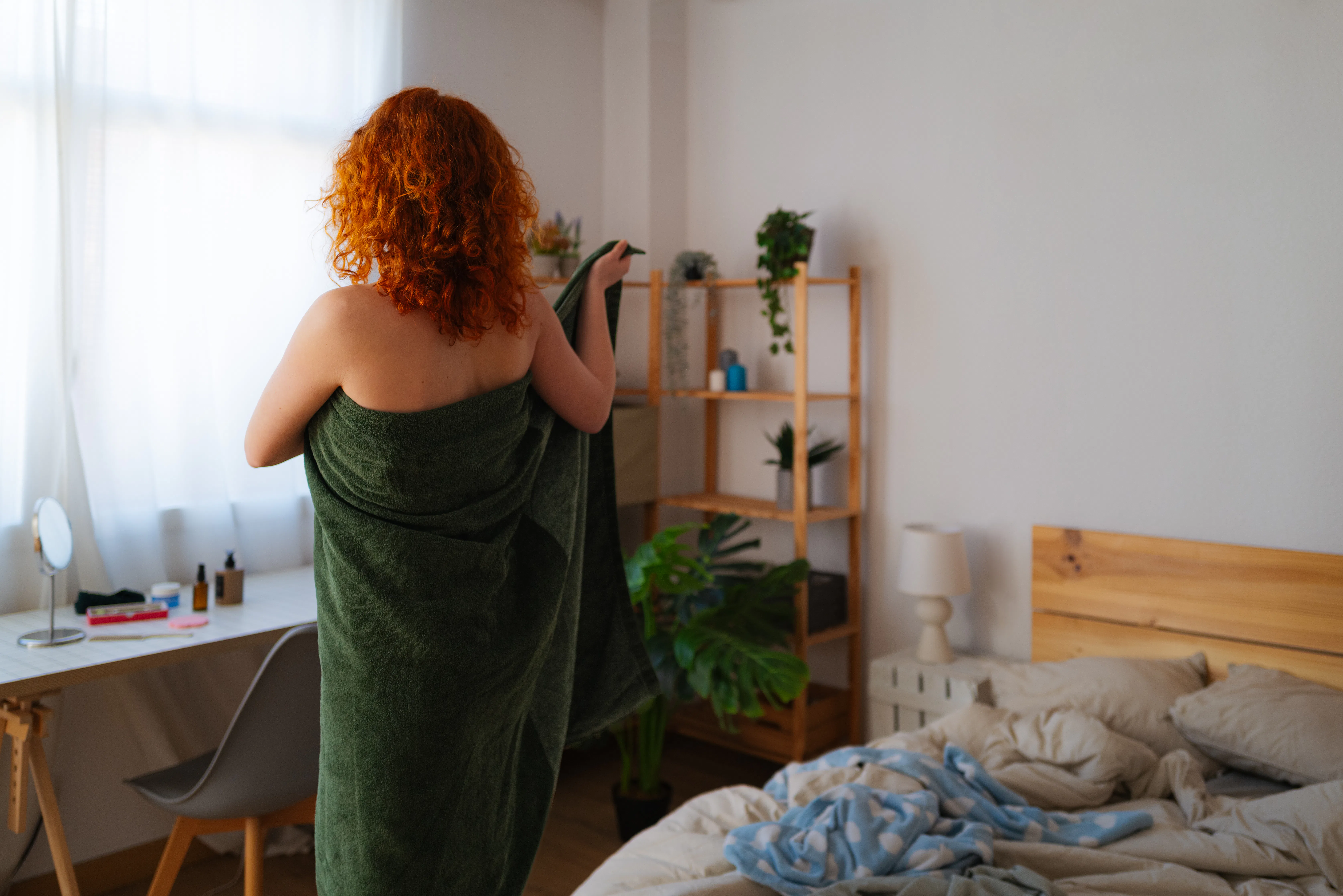 Young redhead stands confidently in bedroom, wrapping towel around body after shower. She embraces m...