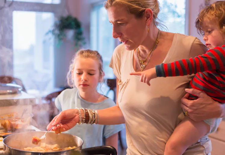 Exhausted mom cooking dinner with her two kids close by in a story about dealing with the monotony o...