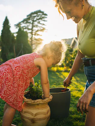 Mother and toddler daughter plant in planter in backyard at sunset, Lugano, Ticino. The photo matche...