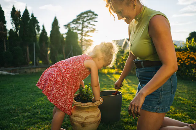 Mother and toddler daughter plant in planter in backyard at sunset, Lugano, Ticino. The photo matche...